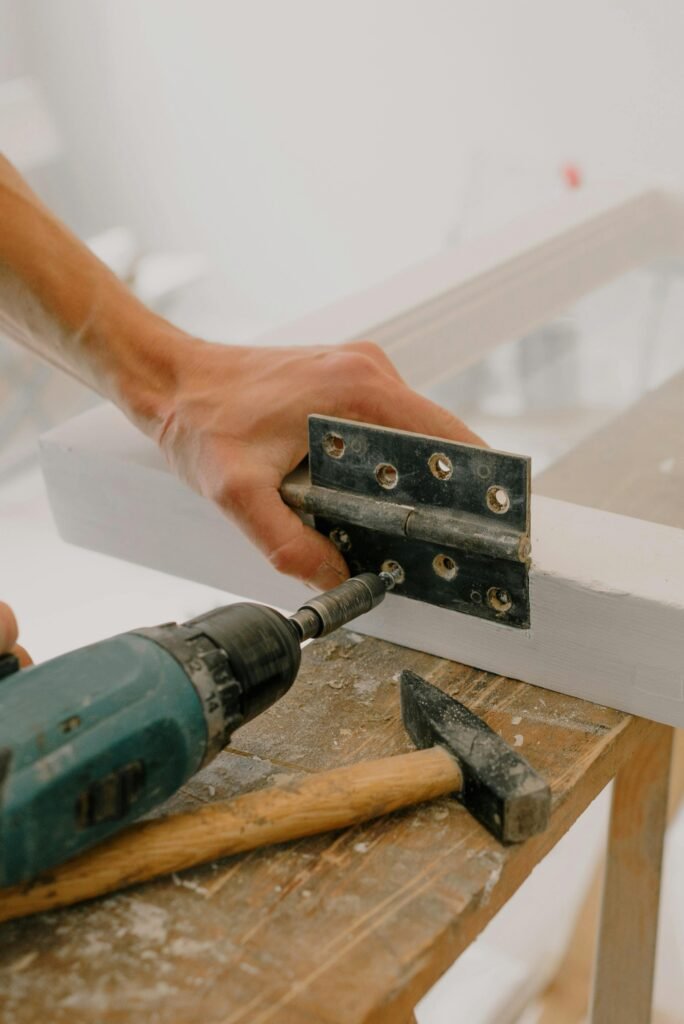 A handyman using a drill to install a hinge on a window frame indoors.